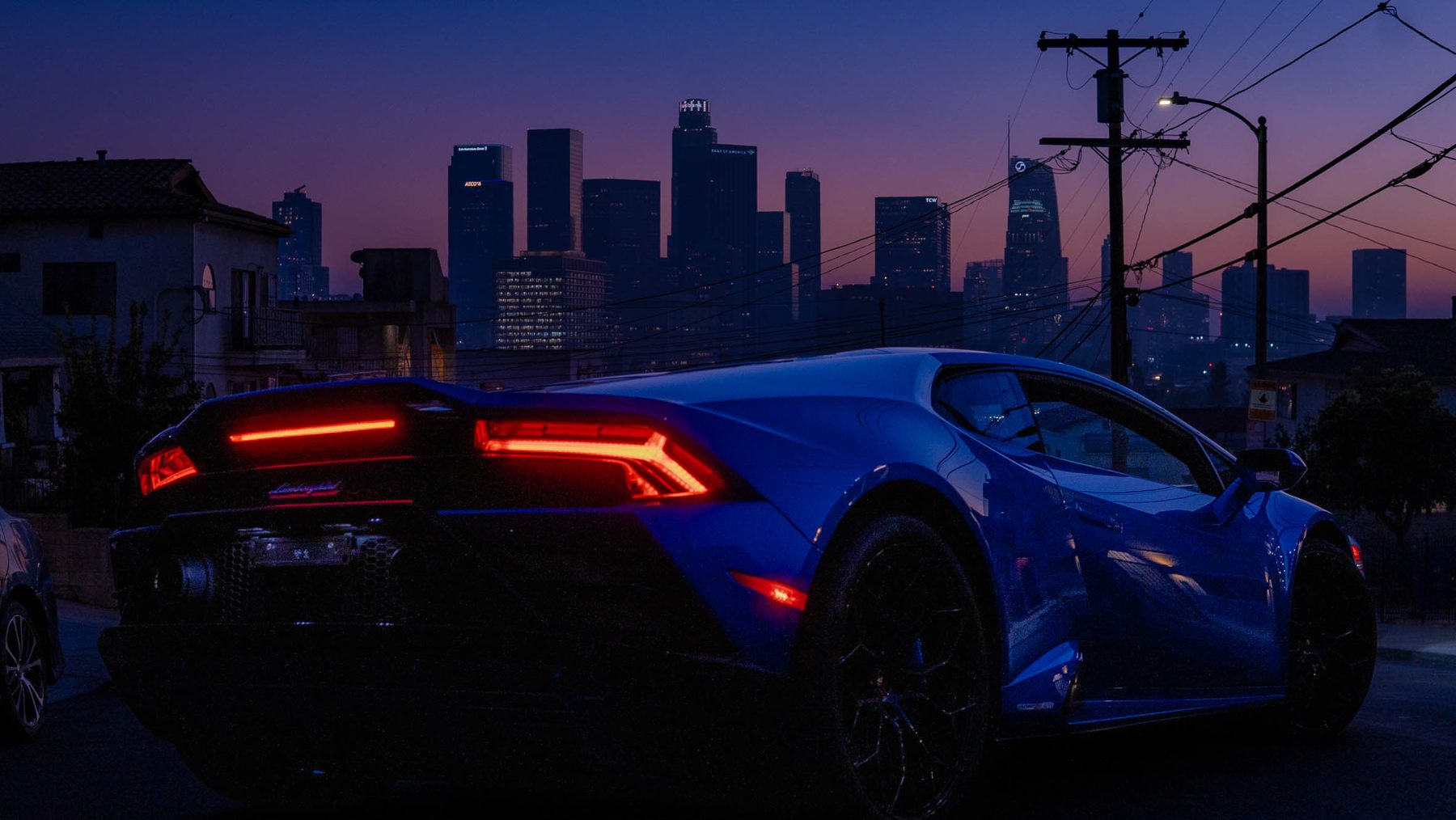 Rear view of a blue Lamborghini glowing against the LA skyline