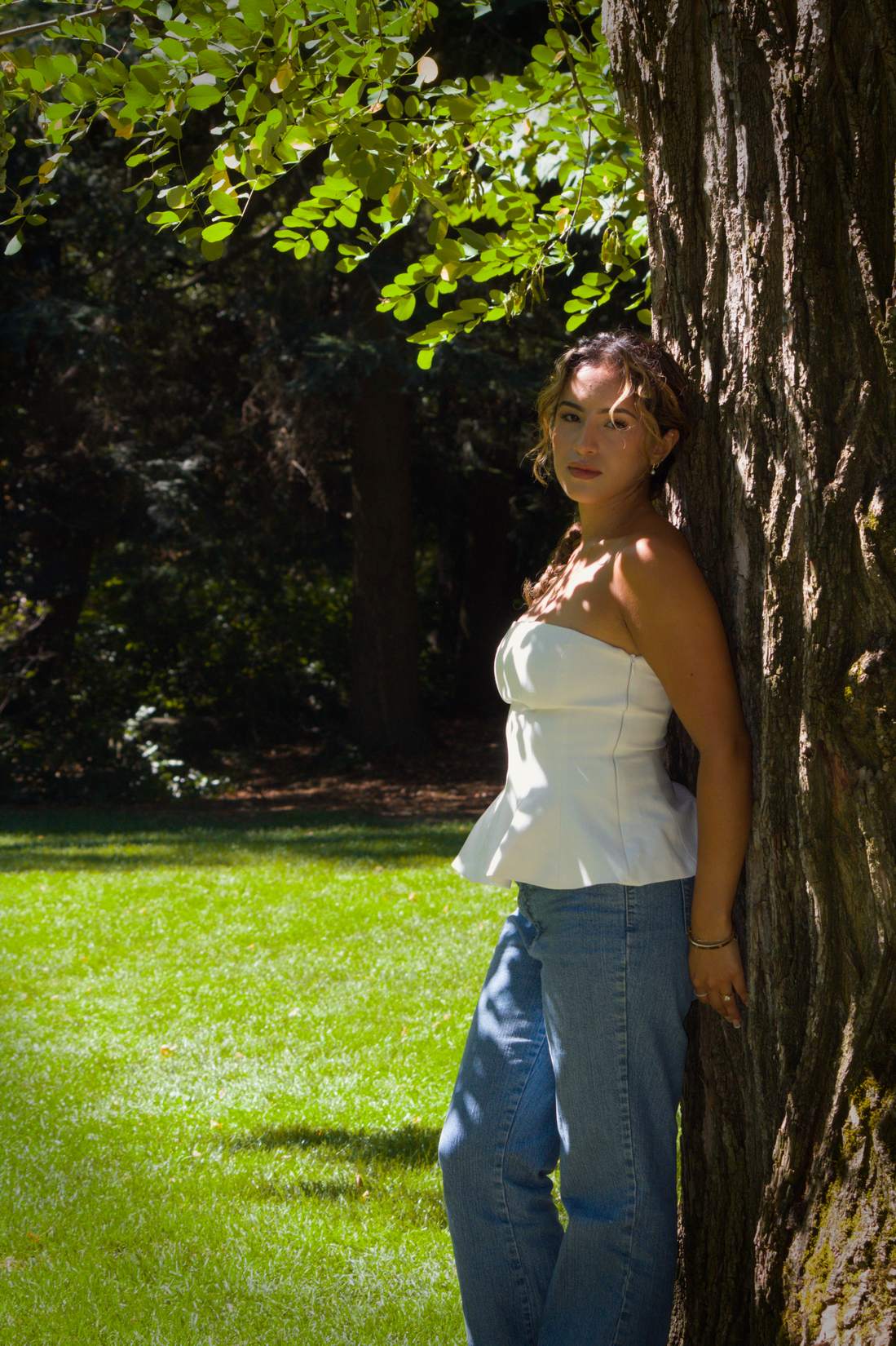 Woman in jeans leaning against a large tree