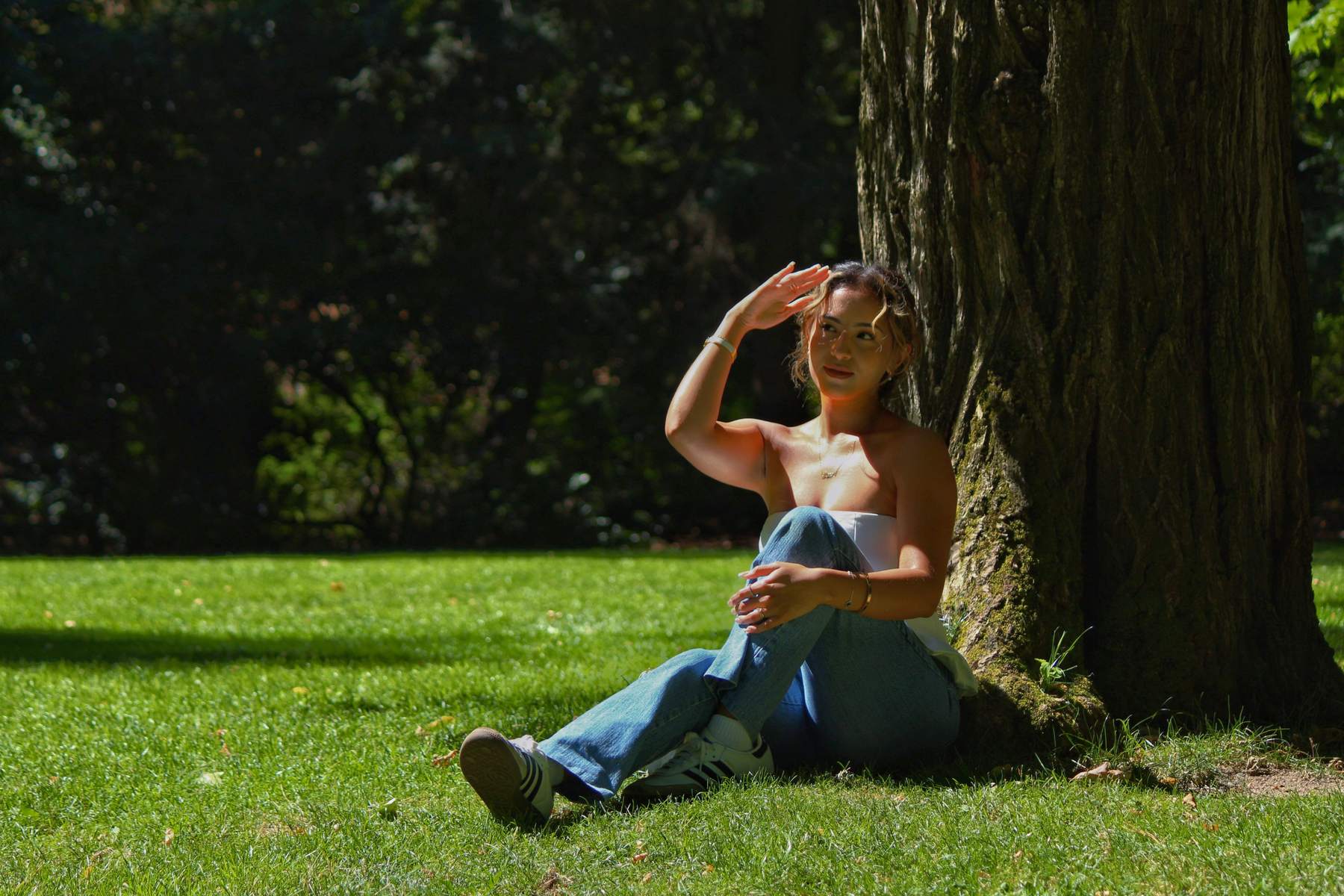Woman sitting under a tree shielding her eyes from the sun