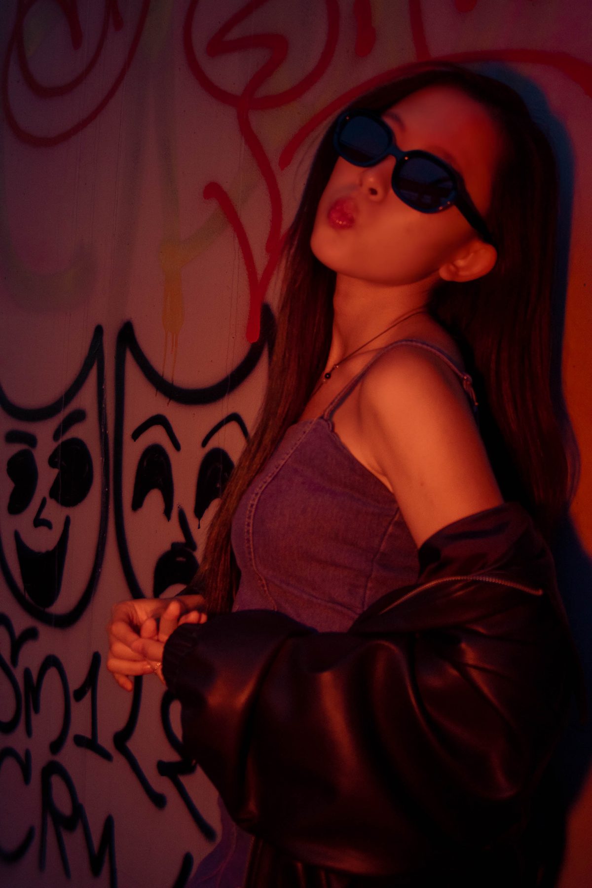 Woman in sunglasses in red light against a graffiti wall