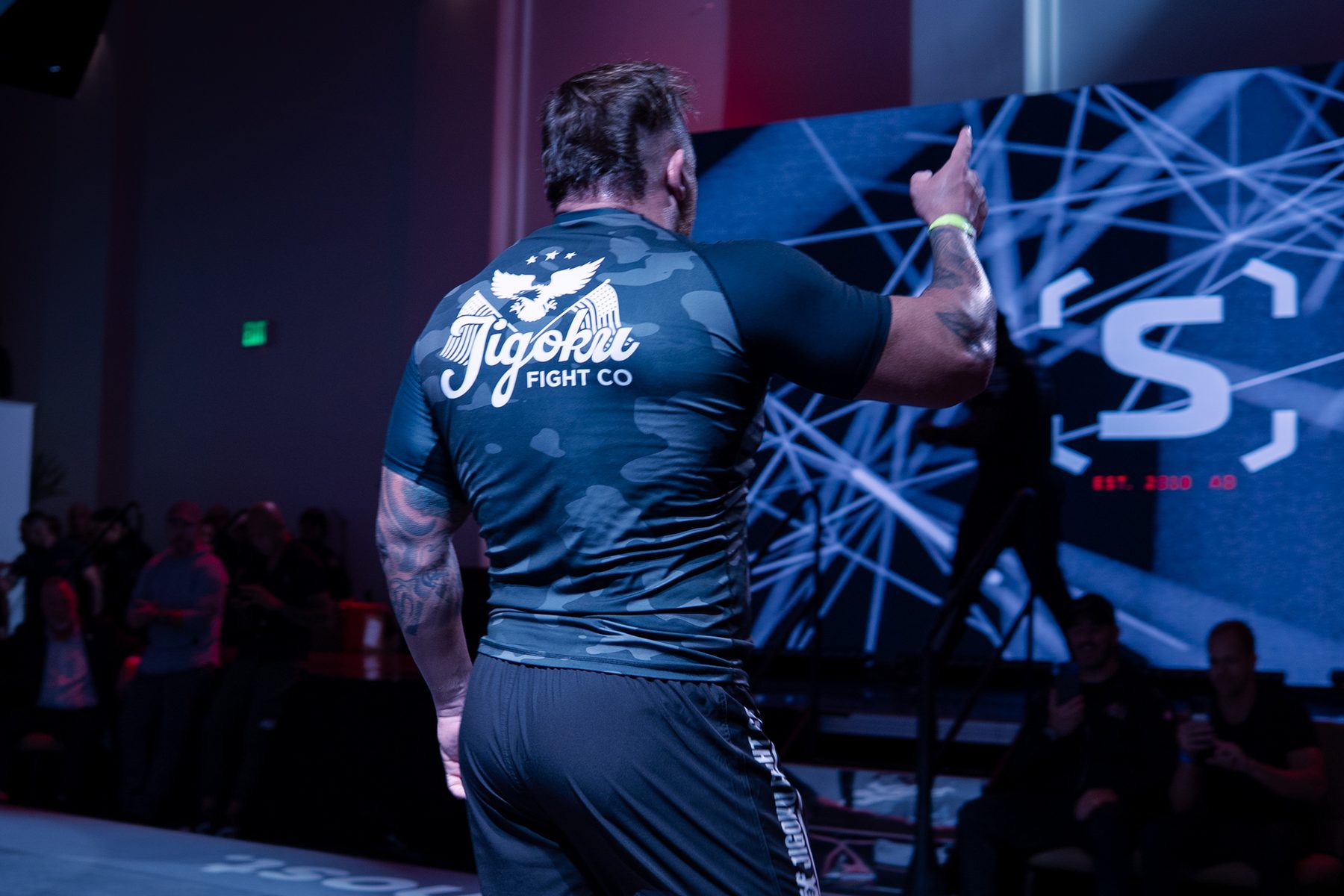 Fighter in a Jigoku Fight Co shirt flexing in front of the stage lights